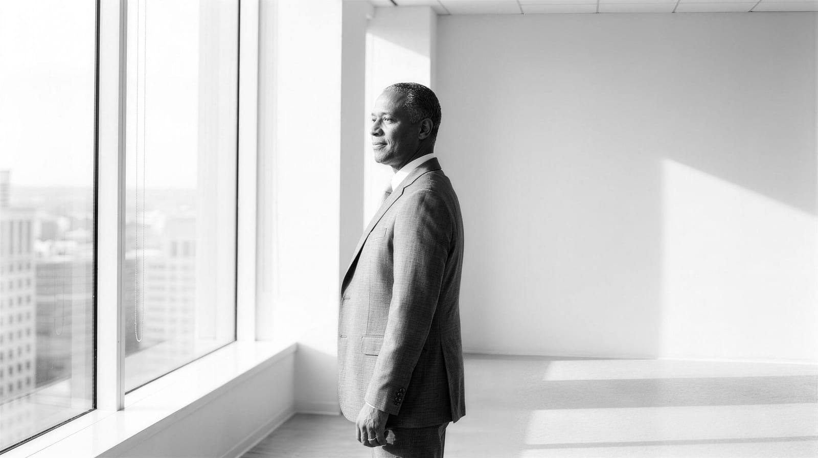 Editorial black-and-white image: an executive at a boardroom table facing an empty chair, AI as a thinking partner before a decision.